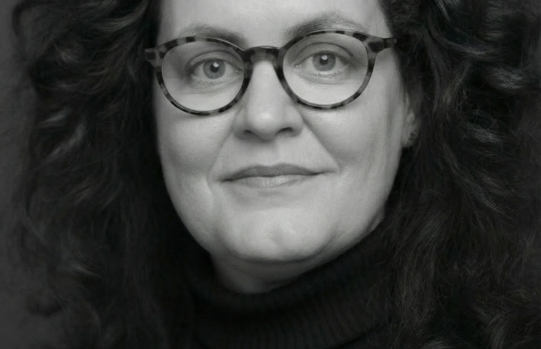 Cornelia Schmitz - Erfahren im Umgang mit der menschlichen Seite von Firmenfusionen. Frau mit langen, lockigen Haaren und Brille, die freundlich lächelt.