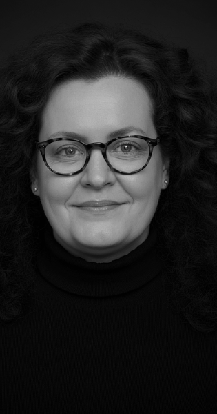 Cornelia Schmitz - erfahrene Mentorin, Coach und Sparring für Führungskräfte. Porträt von Cornelia Schmitz, freundlich lächelnd. Sie hat lockiges Haar und trägt eine Brille.