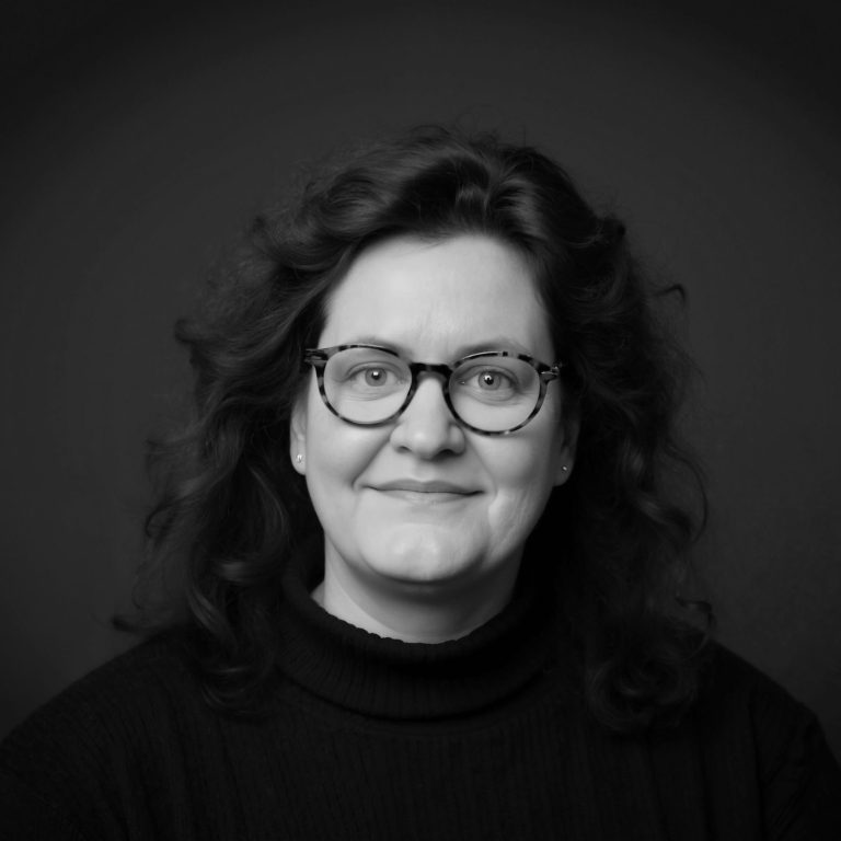 Cornelia Schmitz, eine Frau mit lockigem, schulterlangem Haar und Brille, mit freundlichem und zuversichtlichem Lächeln.