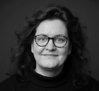 Cornelia Schmitz - erfahrene Mentorin, Coach und Sparring für Führungskräfte. Porträt von Cornelia Schmitz, eine Frau mit lockigen Haaren und Brille, freundlich lächelnd mit offenem Blick.
