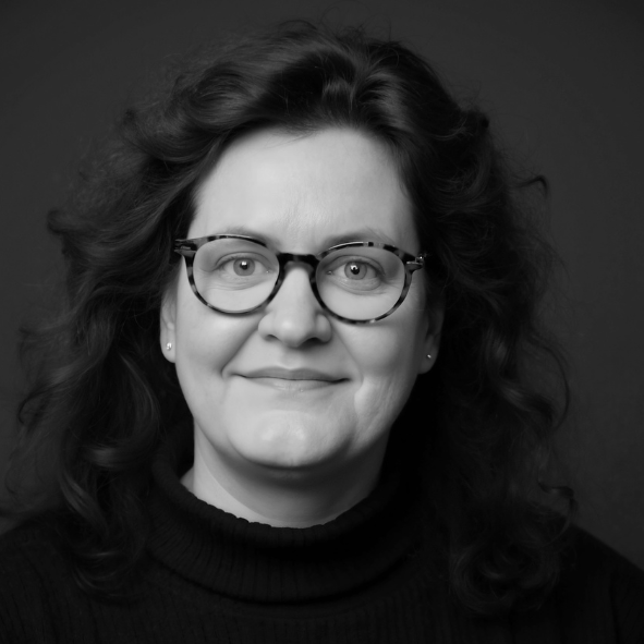 Porträt von Cornelia Schmitz. Frau mit lockigem Haar und Brille, lächelnd und mit klarem Blick.